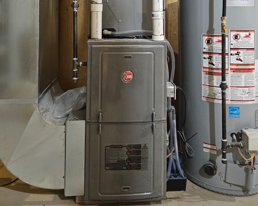 Older gas furnace with PVC venting and water heater beside it, serviced by HVAC Zack in a Durham Region basement.
