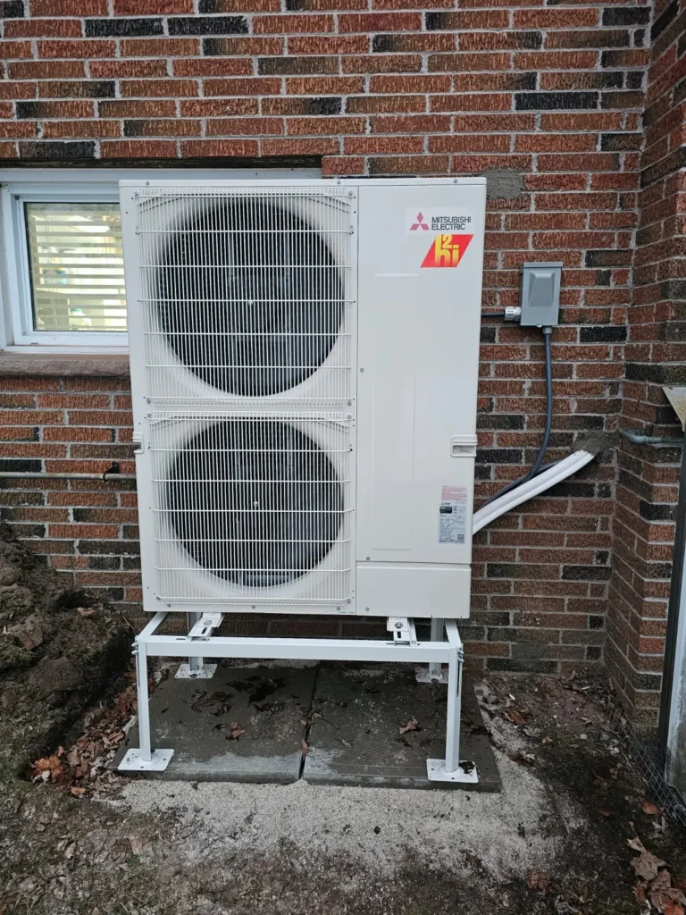 Cold-climate heat pump on a raised stand with weatherproof disconnect installed at an Ontario brick home