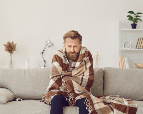 Cold homeowner wrapped in a blanket on a sofa, illustrating a no-heat furnace situation in Durham Region.